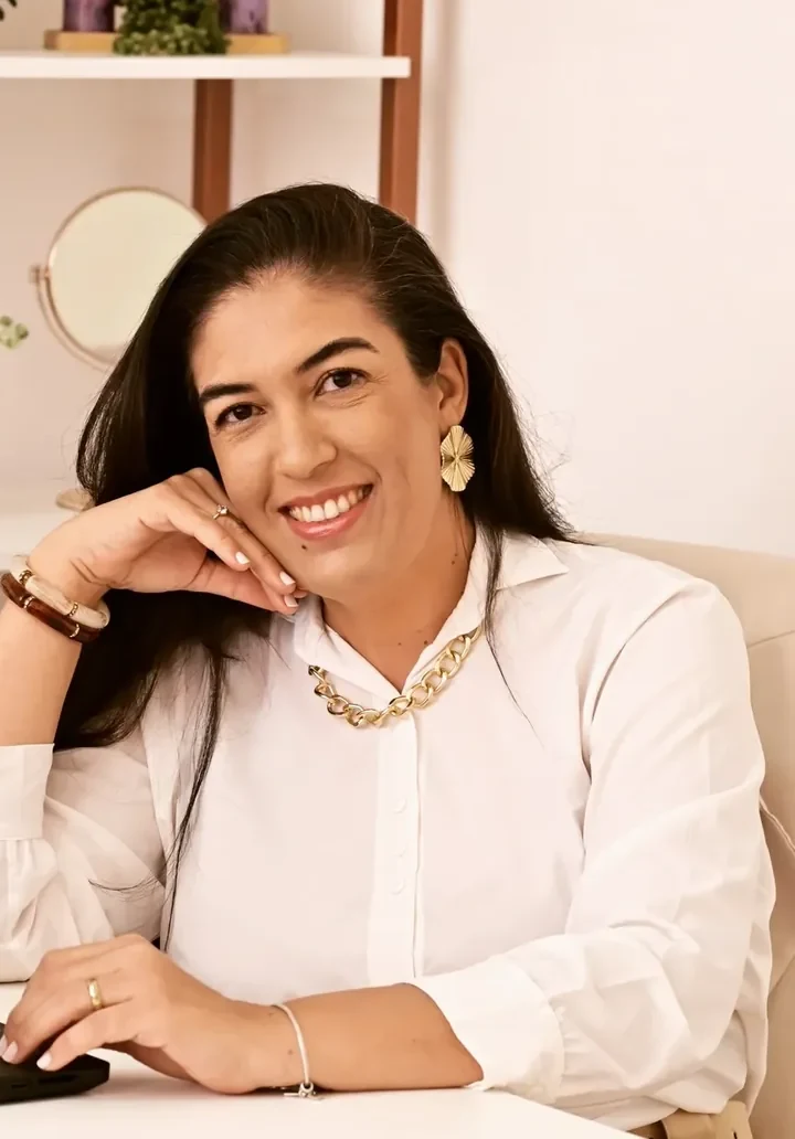 Carolina Vaz Falcon sentada em seu consultório, com plantas ao fundo